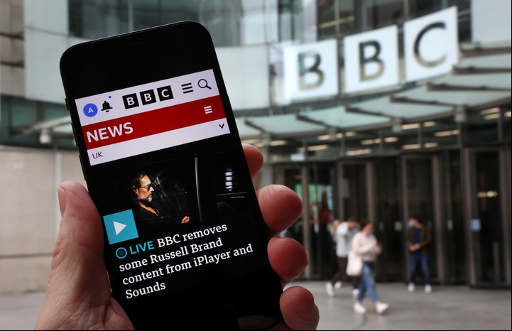 Un celular muestra la noticia sobre la BBC y su decisión de eliminar contenidos con Russell Brand debido a las acusaciones.Foto: EFE