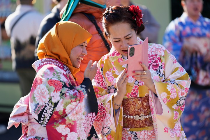 Una mujer de Nagoya, a la izquierda, y su amiga de Tokio, ambas originarias de Indonesia, reaccionan a las fotos que acaban de tomarse mientras visitan el templo budista Sensoji en la víspera de Año Nuevo en Tokio, el martes 31 de diciembre de 2024. (AP Photo/Hiro Komae)